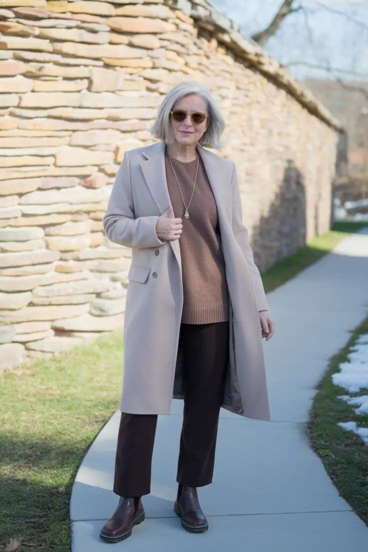 Light gray midi coat with a brown sweater and trousers with brown boots for women over 50 at work