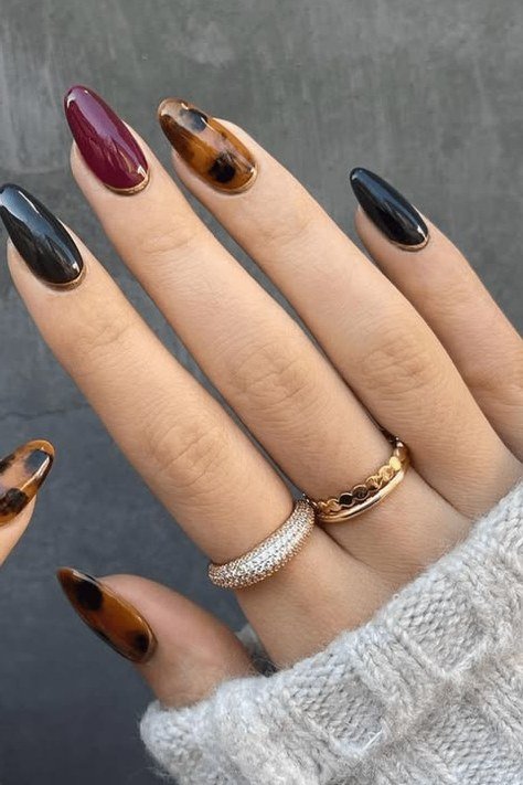Dark plum solid with tortoiseshell accent nails, long almond, glossy, gray sweater cuff, fall nail color for women over 40