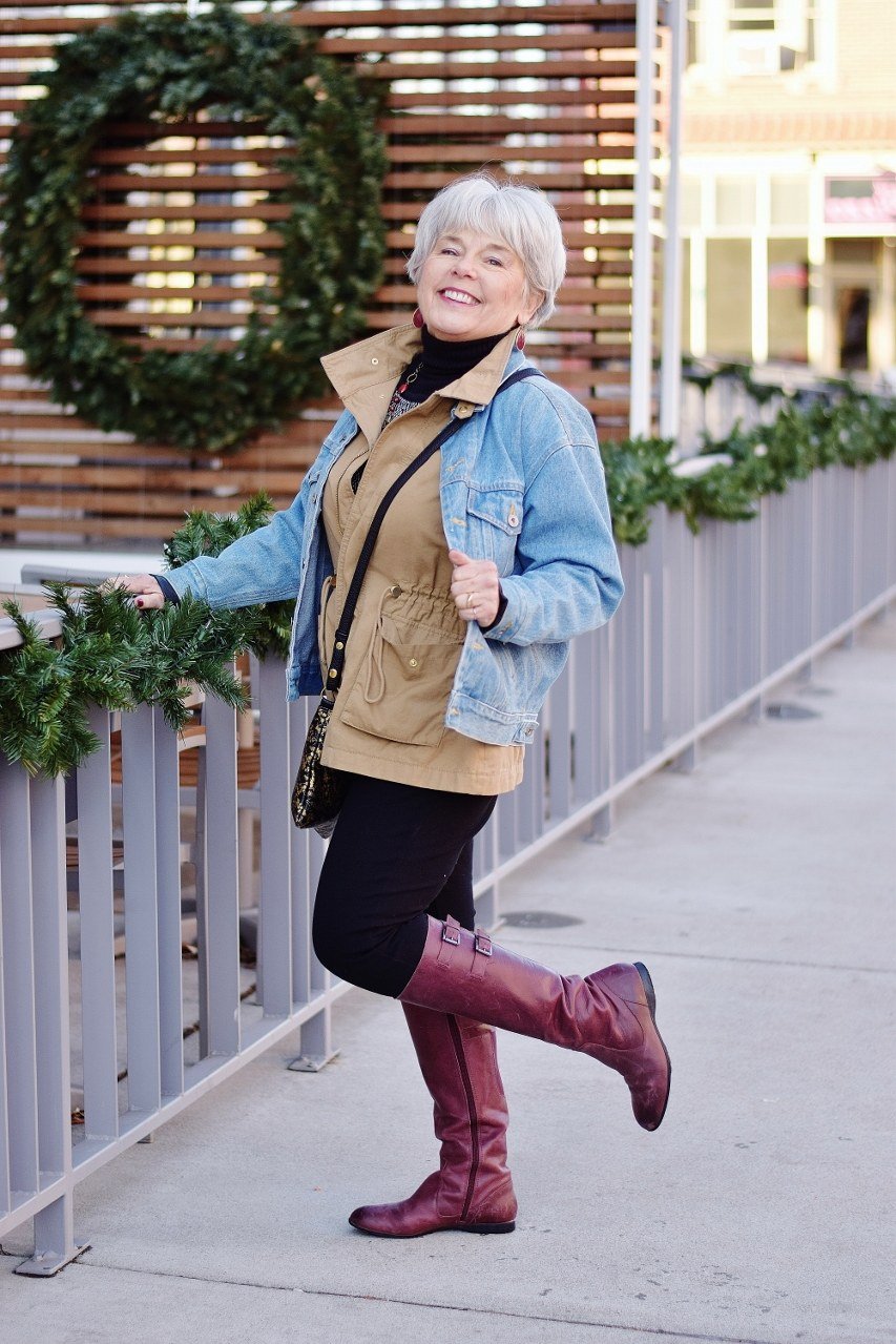 Stylish winter outfit for women over 60: denim jacket with mustard vest and burgundy boots by a wreath