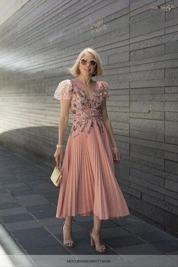 Blonde woman in blush lace top with pleated midi skirt on city street