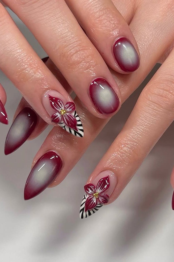 Wine red stiletto nails with an aura ombre effect and floral accent nail, glossy fall drama.