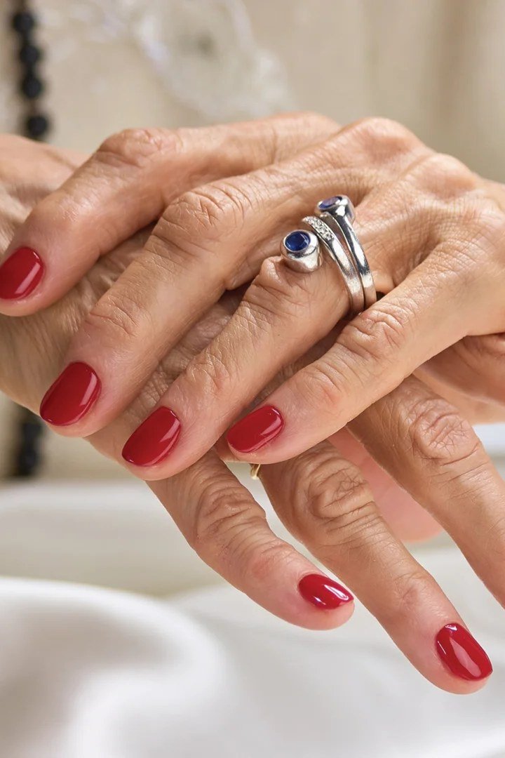 Classic red glossy nails on elderly hands with sapphire ring for women over 70