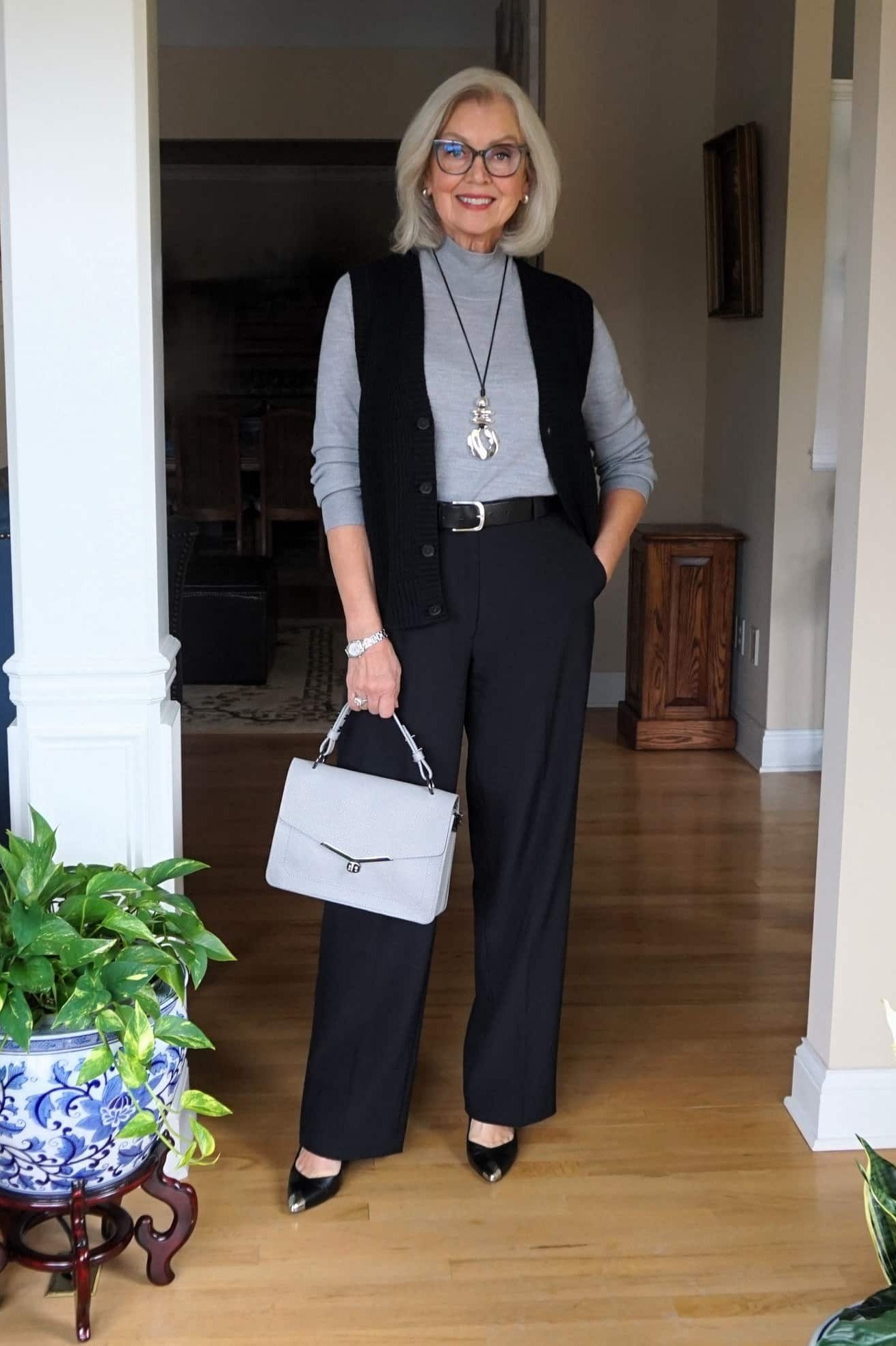 Stylish winter outfit for women over 60: gray sweater vest set with black trousers and white bag