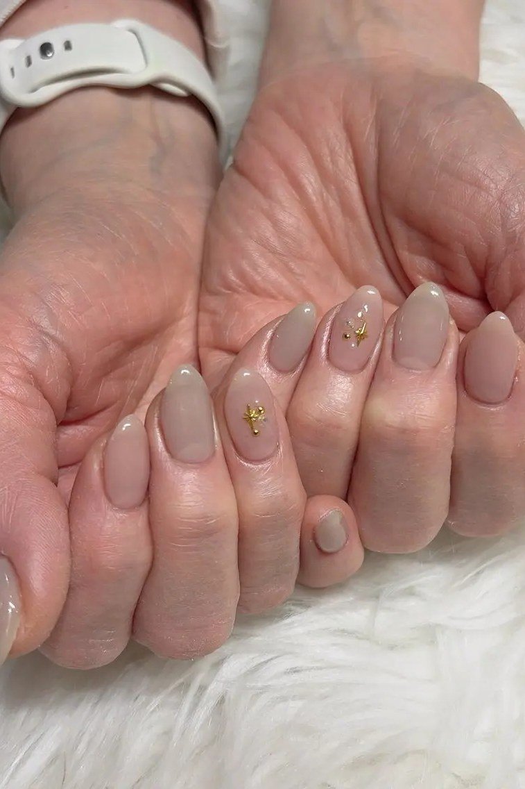 taupe mauve almond nails with gold star accents, celestial nail art for mature hands