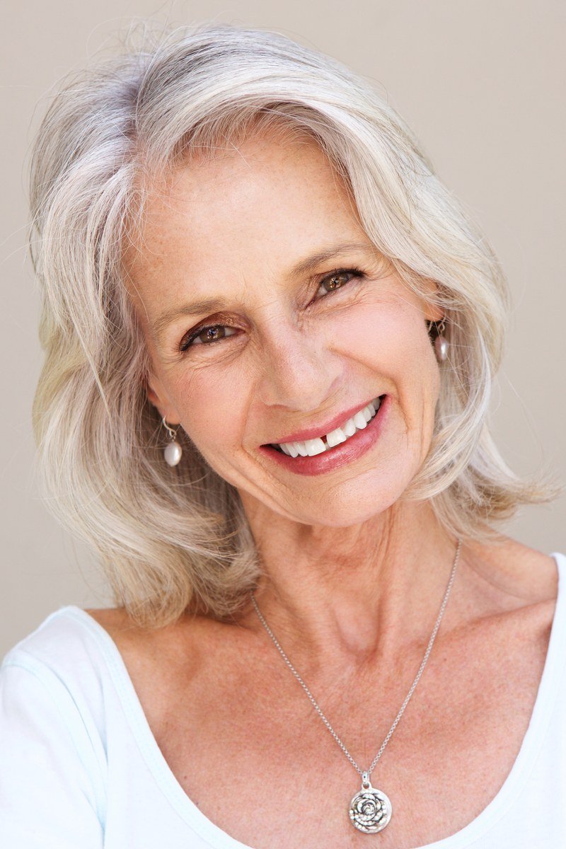 Blonde layered haircut on a smiling older woman, front view, medium hairstyle for women over 60