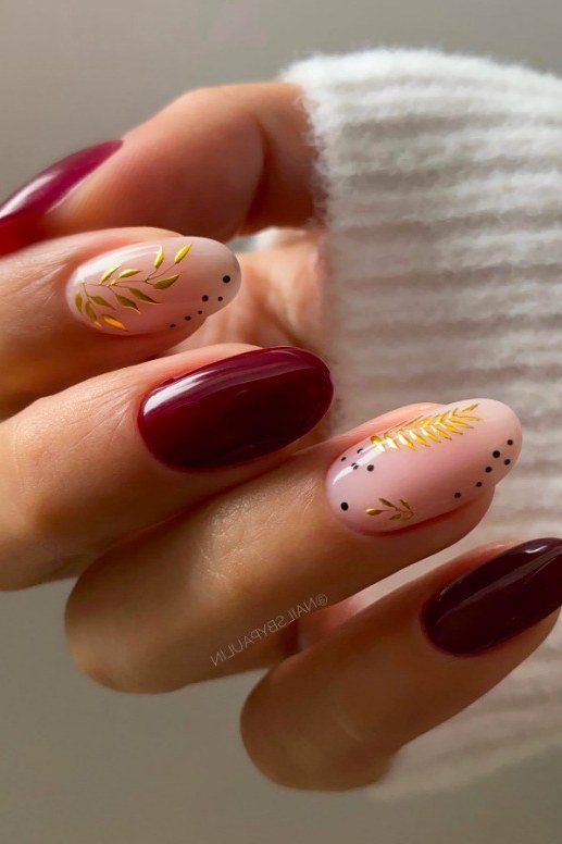 Mix of burgundy and blush pink almond nails with gold leaf accents, glossy fall elegance.