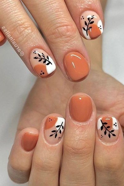 Peachy orange almond nails with black leaf branch art accents, glossy fall design.