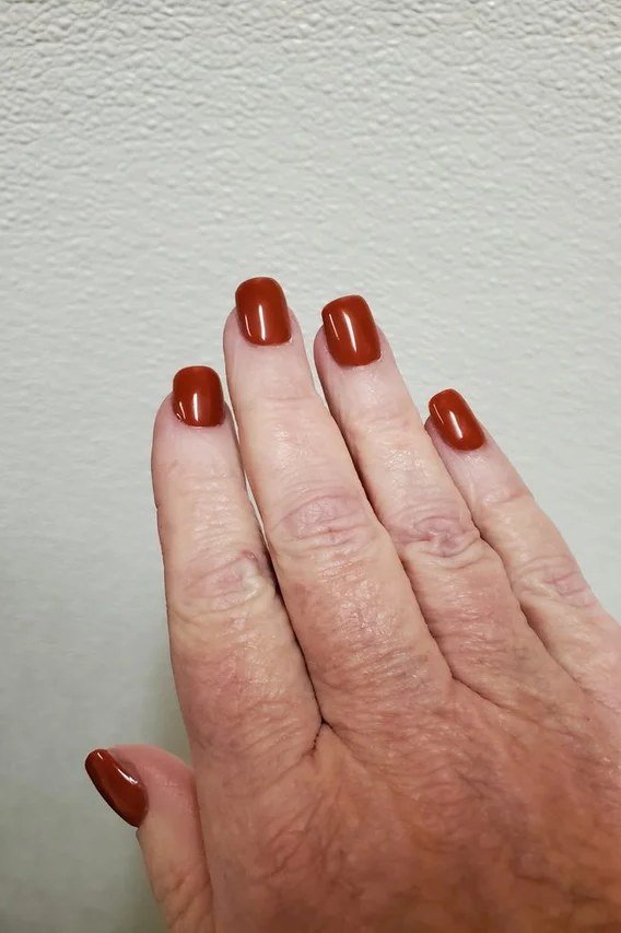 Burnt orange rust nail polish on an older hand