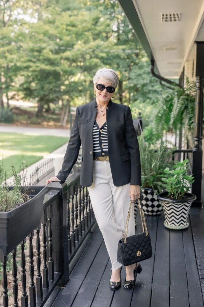 Woman over 50 in a black blazer with a striped top and cream trousers