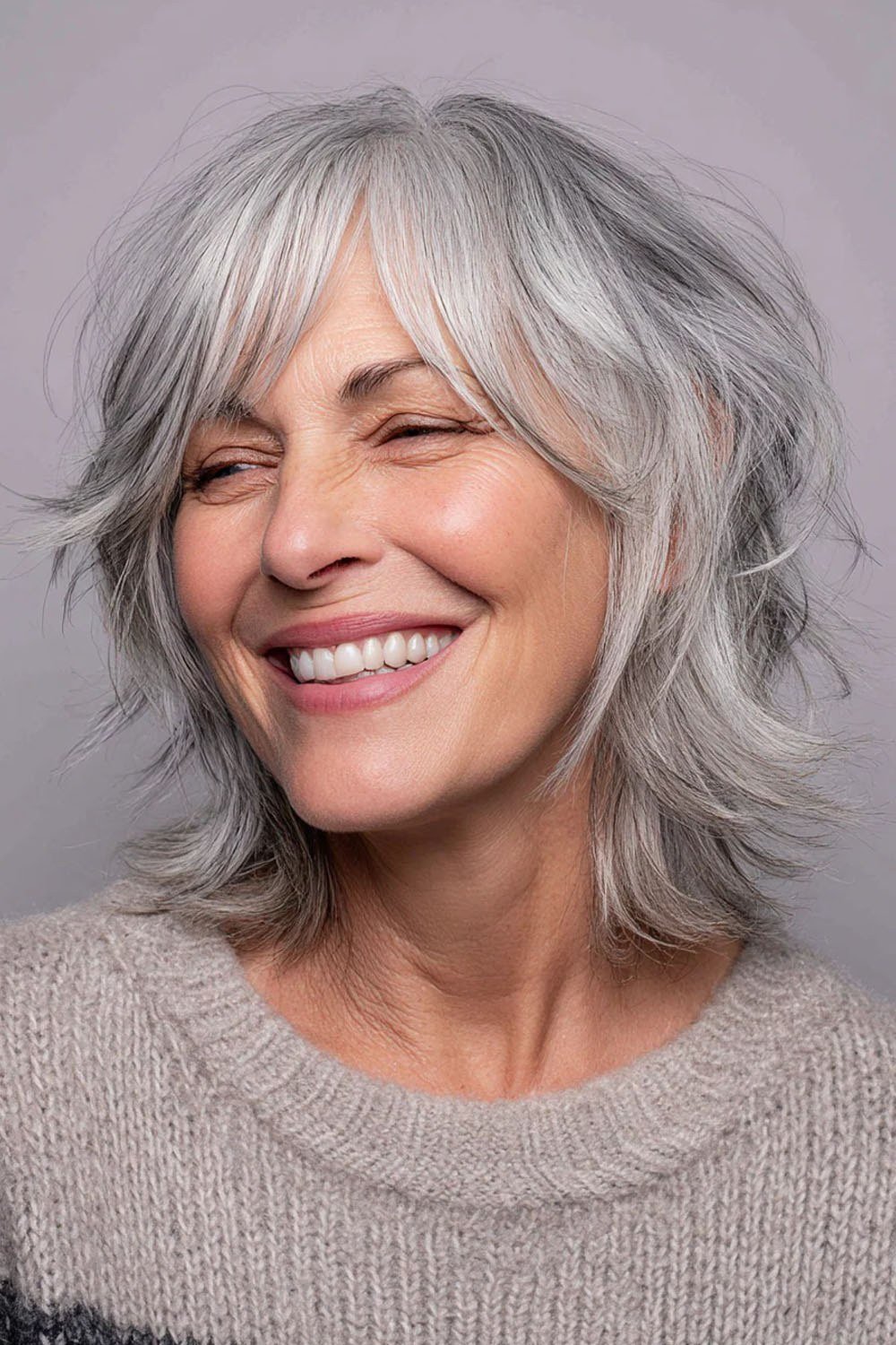 Wavy silver-gray hair with bangs on a smiling older woman, front view, medium hairstyle for women over 60