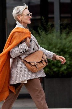 older woman in bright orange wrap scarf cape over beige outfit, street