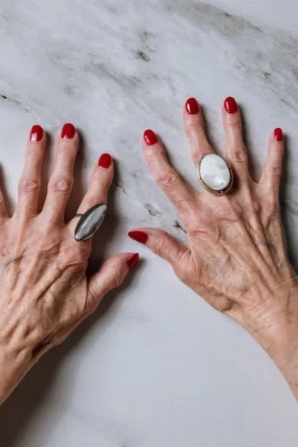 Red nails paired with statement rings on mature hands