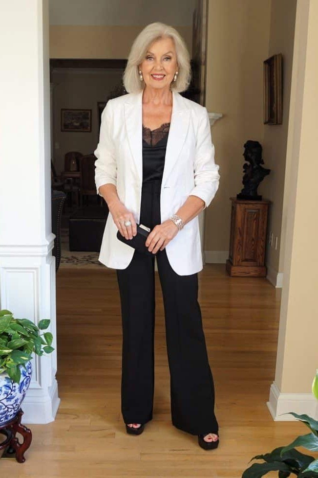 Woman over 50 wearing a white blazer with a black top and black wide leg trousers