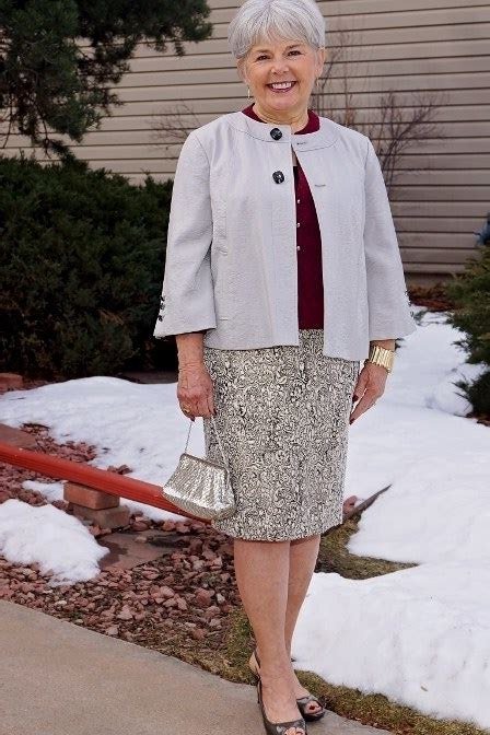 Stylish winter outfit for women over 60: light gray jacket over burgundy top with tweed skirt in snow