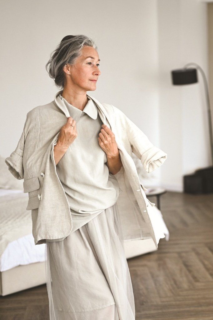 Older woman with an ivory cardigan draped over her shoulders with ivory trousers and a neck scarf