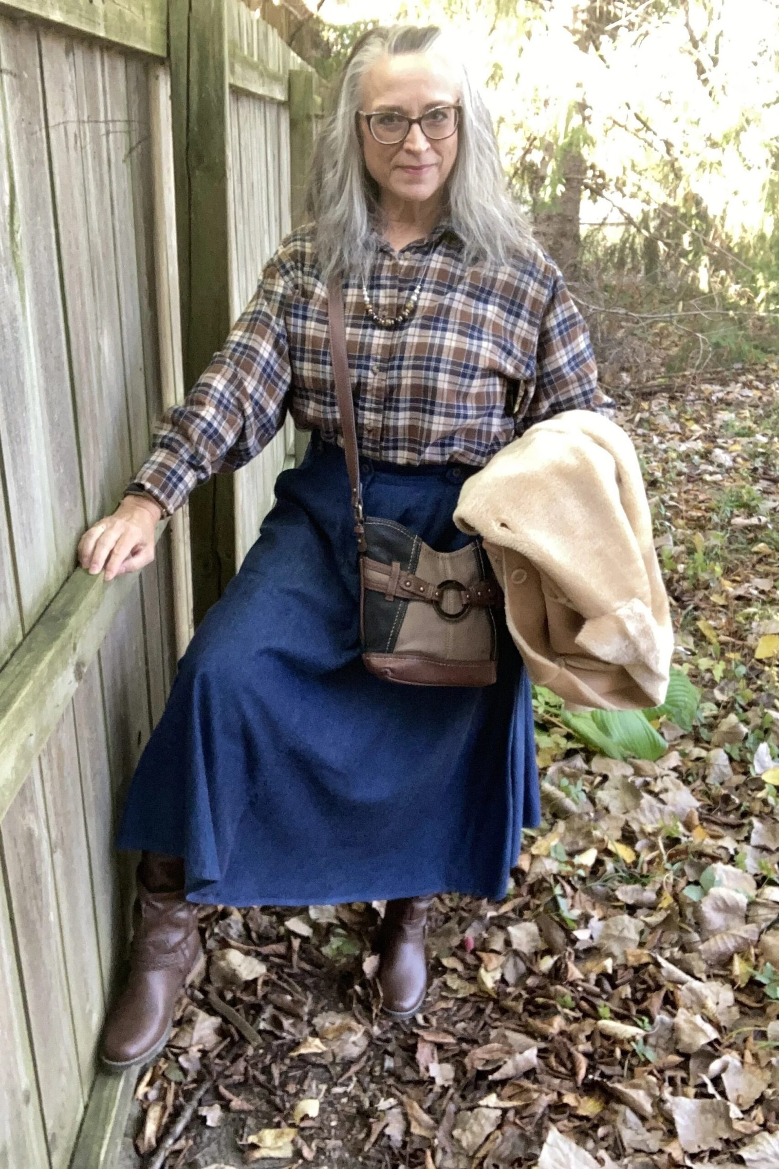 Plaid shirt with a denim midi skirt, brown boots, and a cream sweater over the shoulders, rustic weekend outfit for women over 40