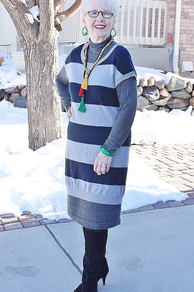 Stylish winter outfit for women over 60: striped sweater dress with black tights and boots in snow