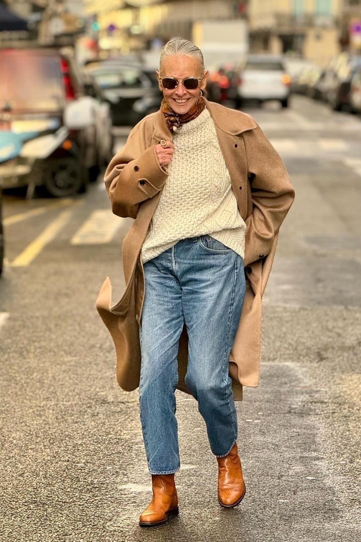 Fall city outfit for women over 50: camel coat cream sweater blue jeans tan boots
