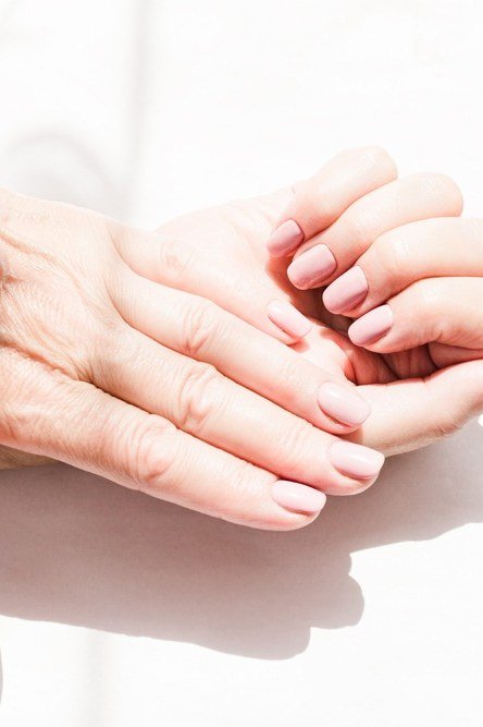Older hands with milky white nails glowing in sunlight