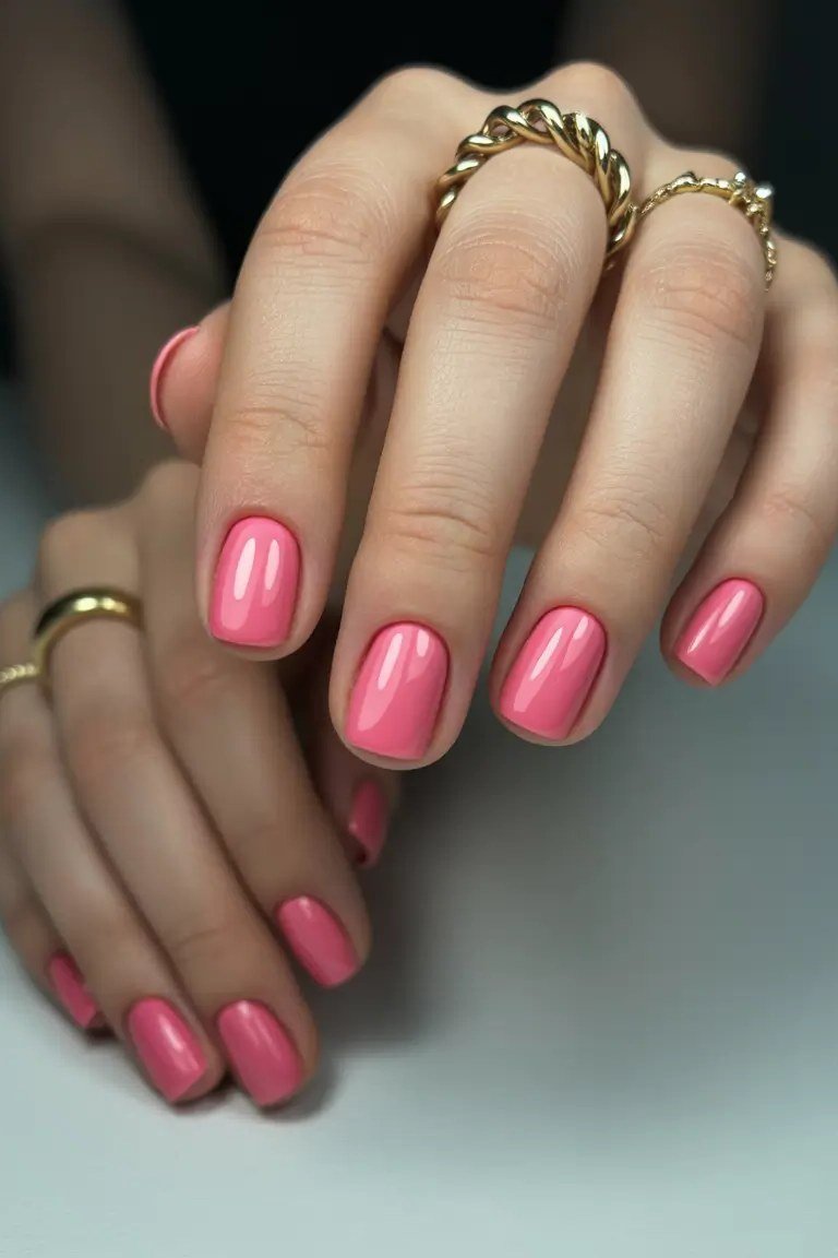 Vivid pink nail polish with gold rings, hands gently clasped