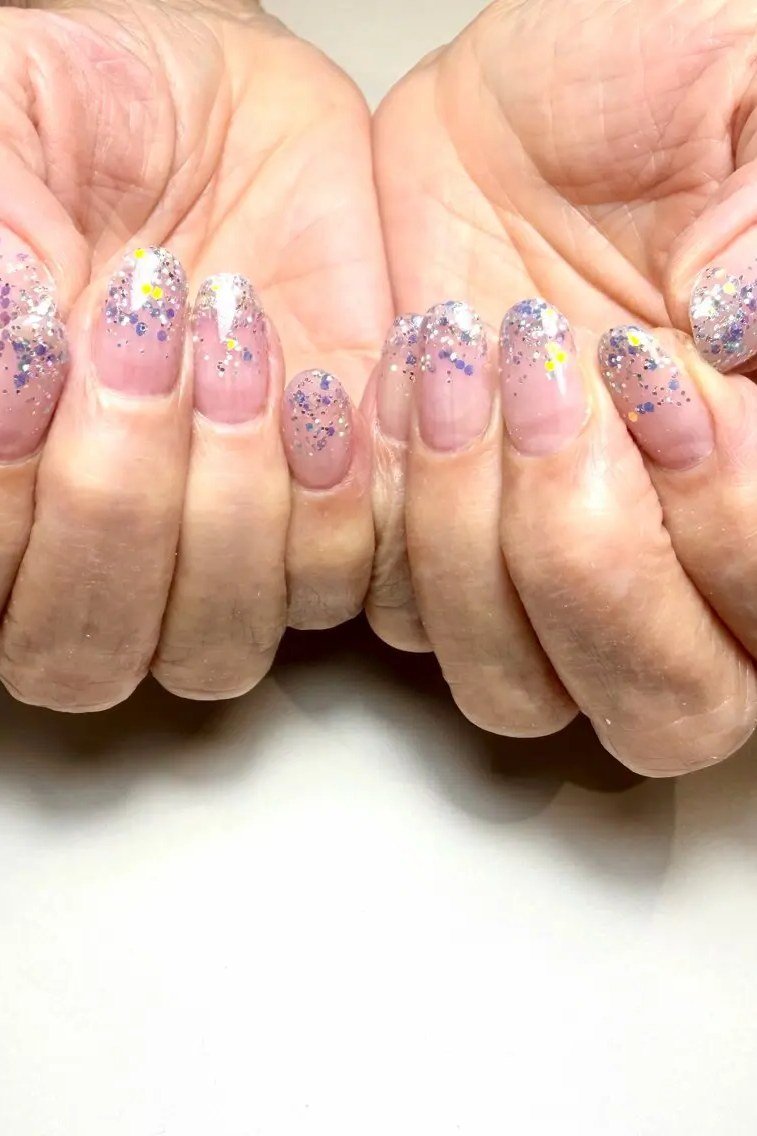 Pink nails with confetti glitter on clasped hands for women over 70