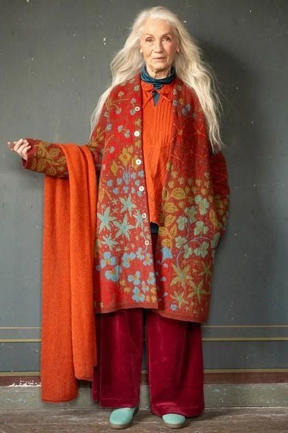 older woman in orange floral long coat with red pants, studio portrait