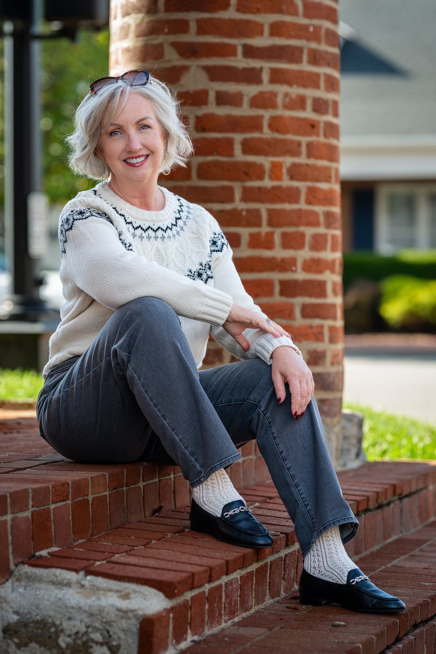 Fair isle sweater with gray jeans, seated on brick steps