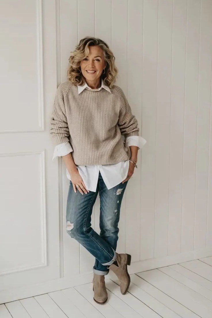 Casual fall outfit for women over 60: tan suede boots, fringe bag, cream sweater, indigo jeans