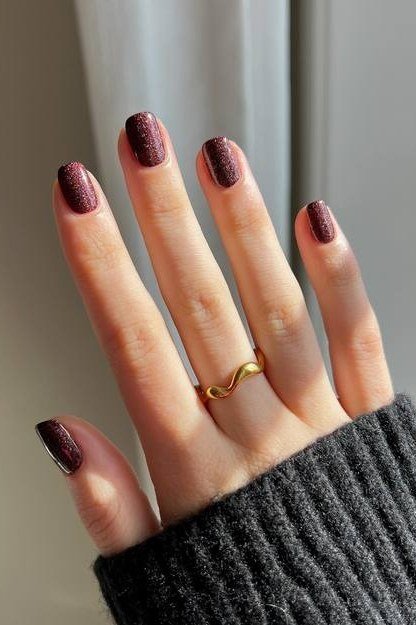 Deep plum short oval nails peeking from a grey knit sweater cuff, glossy moody fall.
