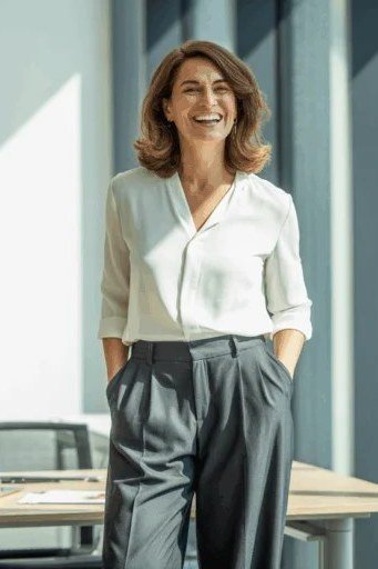 Woman over 50 in a white blouse with gray pleated trousers at the office