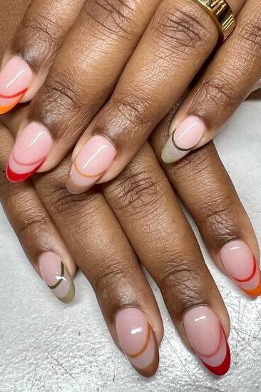 Nude almond nails with red outlined french tips on mature dark skin hands, glossy fall accent.