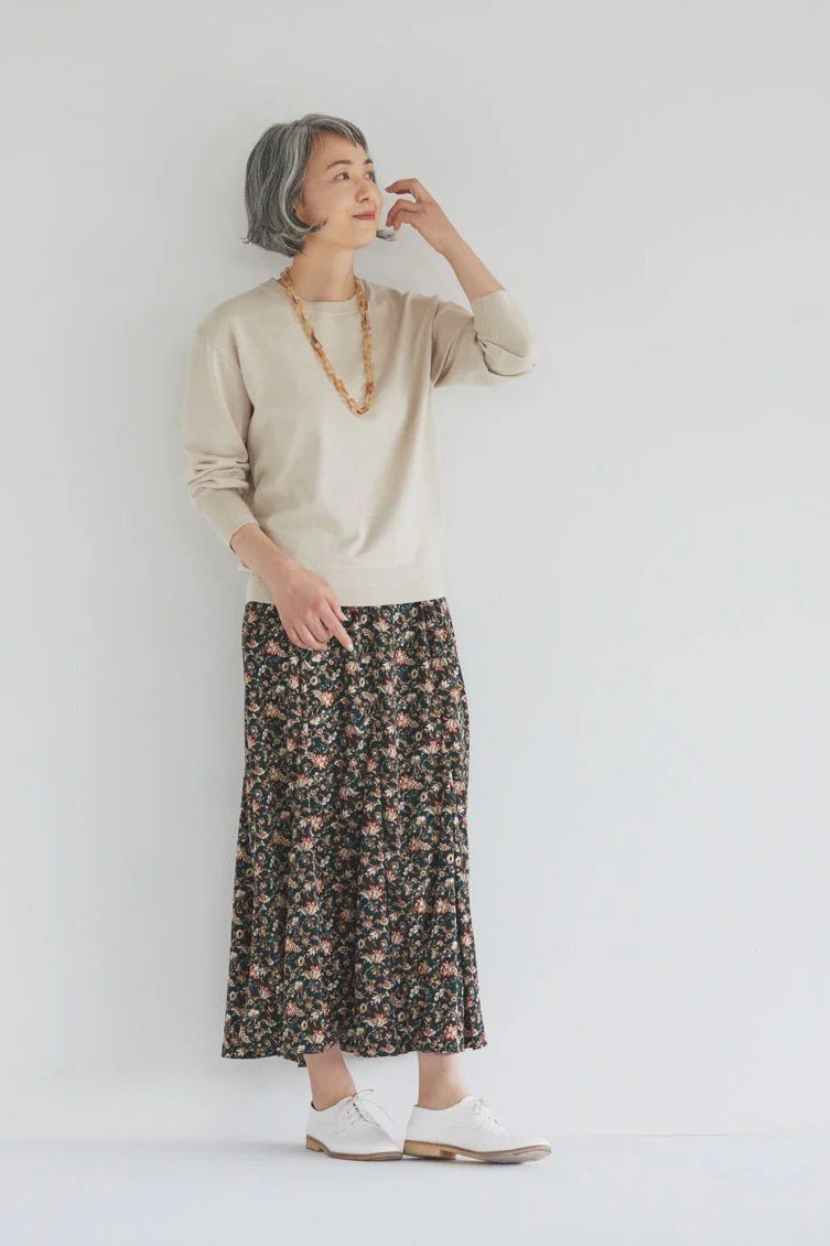 Older woman wearing a cream top with a floral midi skirt and white sneakers
