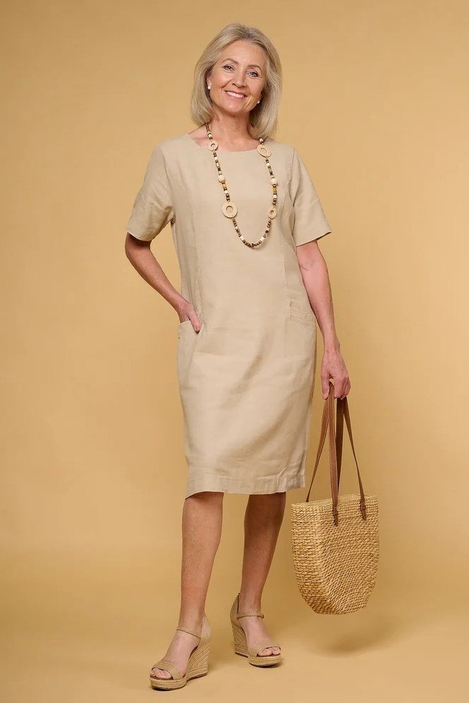 Woman in a beige linen midi dress with a straw tote, studio shot - summer dress for women over 50