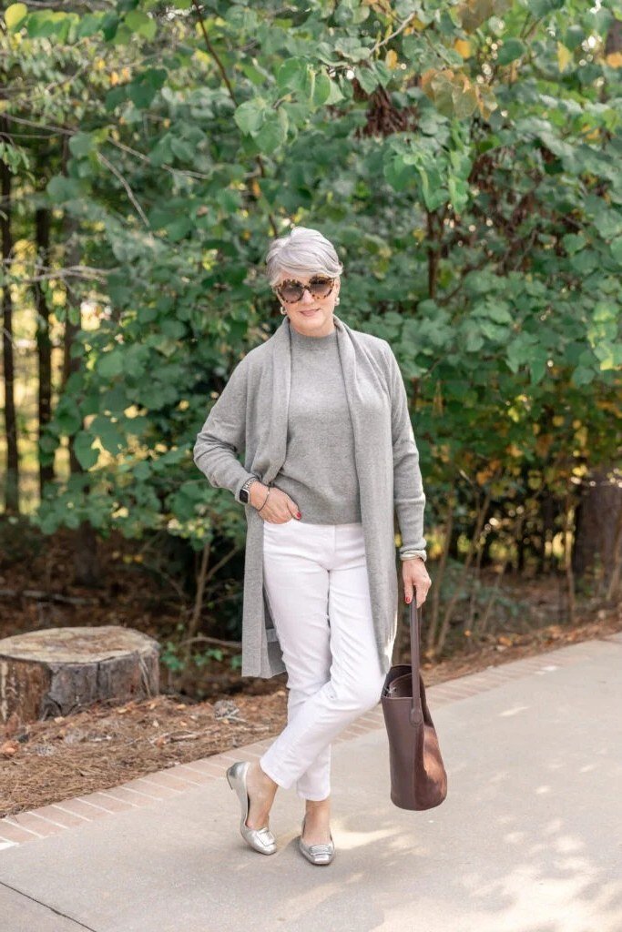 Woman over 60 wearing gray cardigan, white jeans, beige heels, garden path