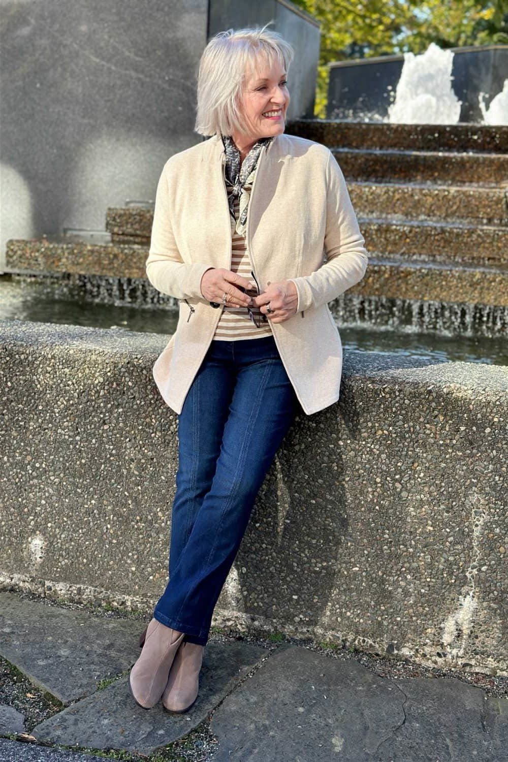 Woman over 60 wearing cream cardigan, striped top, dark jeans, fountain