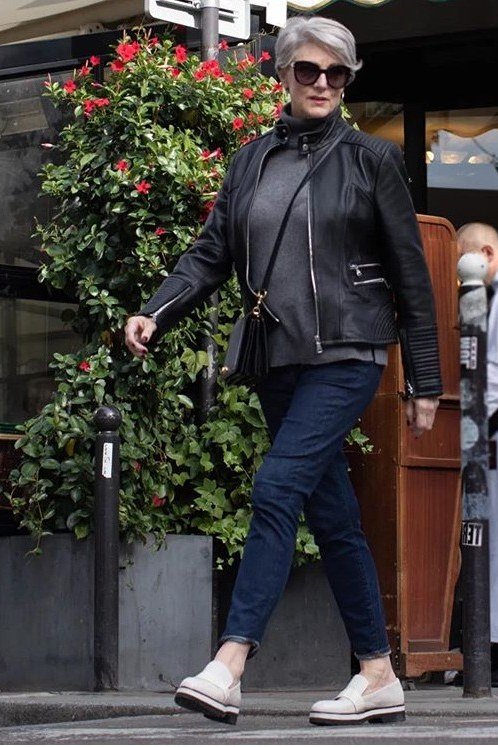 black leather jacket grey top blue jeans white sneakers crossbody bag women over 50