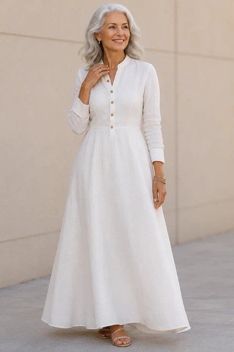 Gray-haired woman in a long white maxi dress with buttons, standing outside a building - summer dress for women over 50