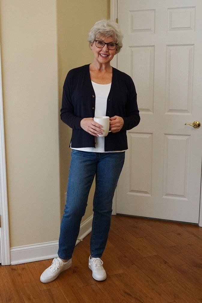 Woman over 60 wearing navy cardigan, white top, medium jeans, white sneakers, doorway