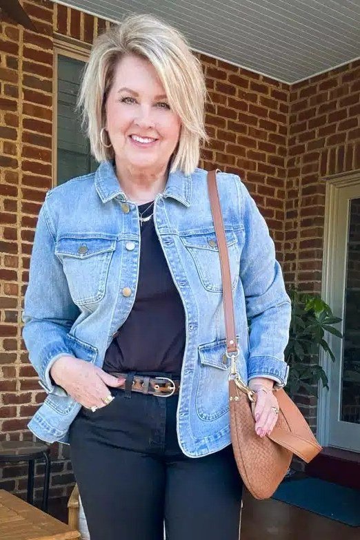 Denim jacket with black top and dark jeans, tan shoulder bag