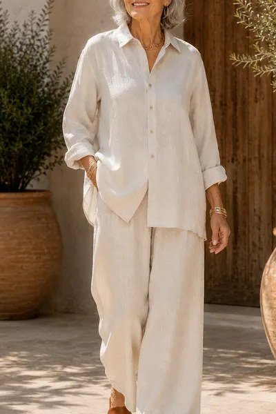 Older woman in a cream linen button-up shirt and wide-leg linen pants standing by terracotta planters, an ageless fashion idea for women over 70