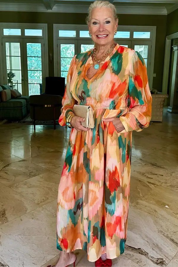 Older woman in a colorful watercolor-print long floral gown shown in a full indoor view, an ageless fashion idea for women over 70