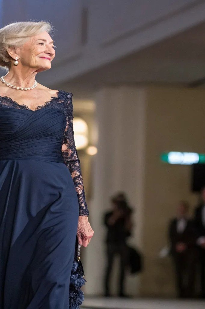 Older woman in a navy lace long-sleeve evening gown walking at night, an ageless fashion idea for women over 70