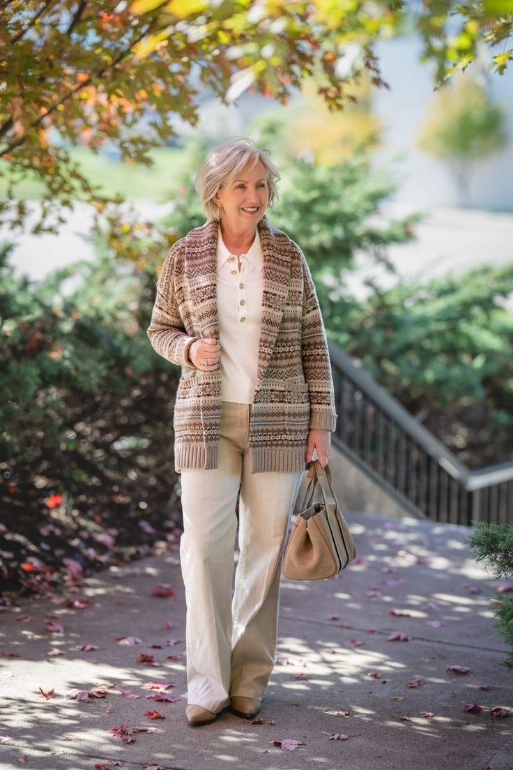 Older woman walking outdoors in a brown plaid cardigan with white pants and a tan handbag