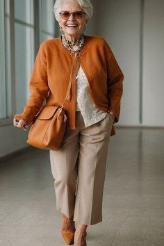 Older woman with sunglasses walking in a rust-orange cardigan with tan pants and a matching rust handbag