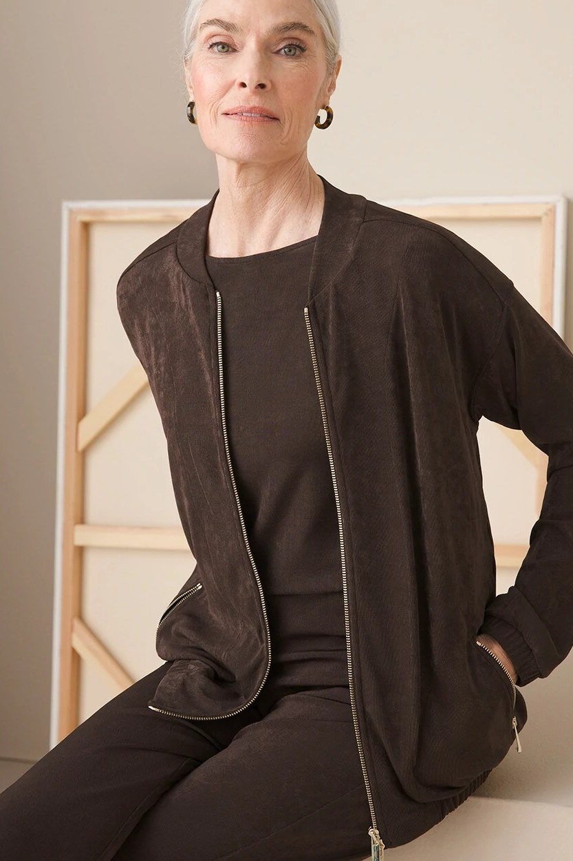 Older woman seated, wearing a dark brown zip-front cardigan with a dark outfit