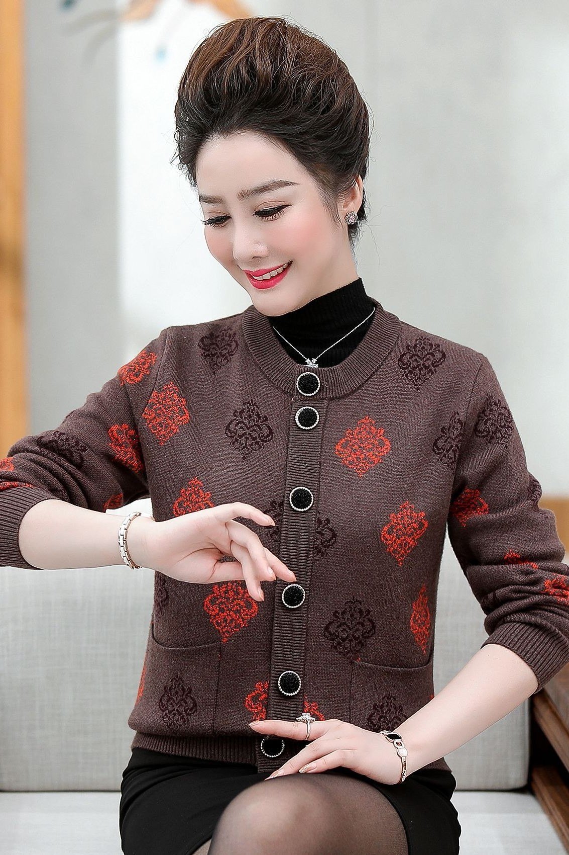 Older Asian woman seated, wearing a brown cardigan with red floral embroidery over a black turtleneck