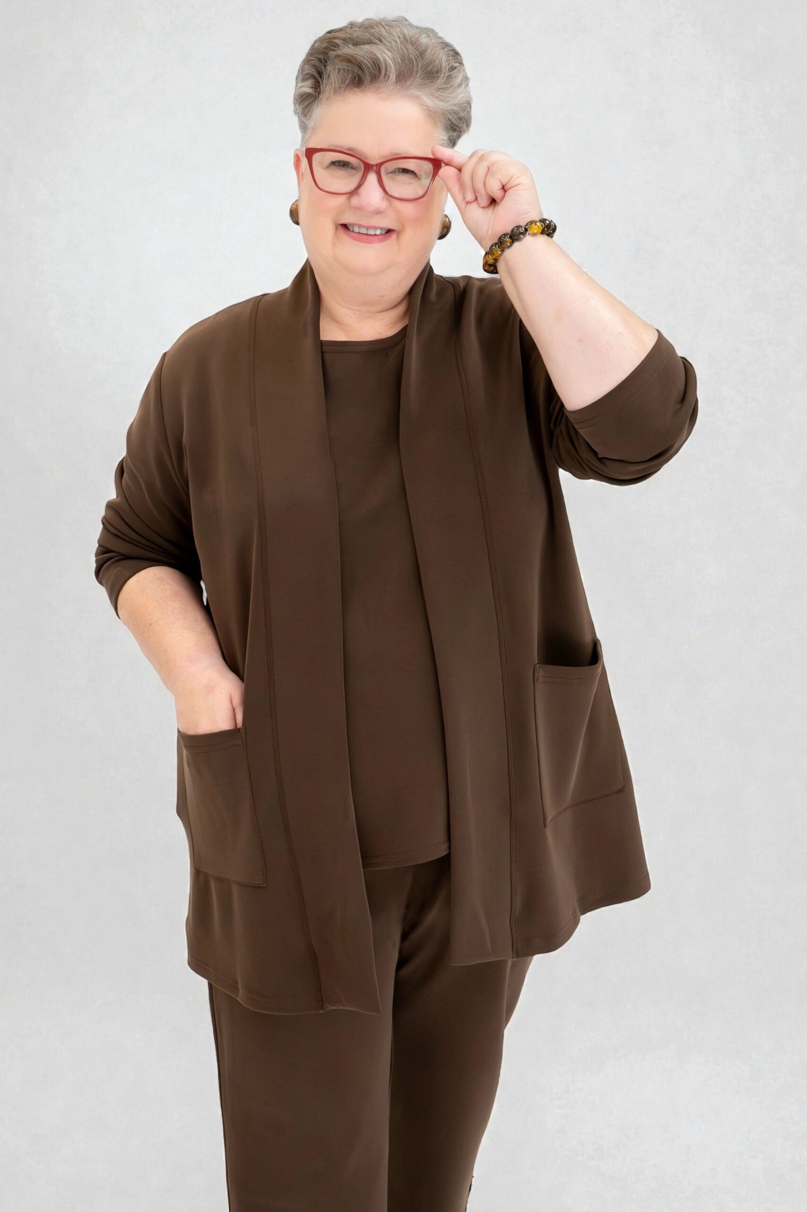 Older woman with glasses in a studio wearing a dark brown open cardigan with a matching knit set