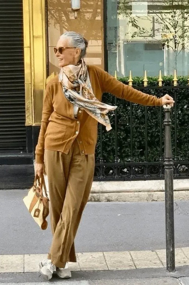 Older gray-haired woman on a street wearing a mustard-tan cardigan set with a scarf