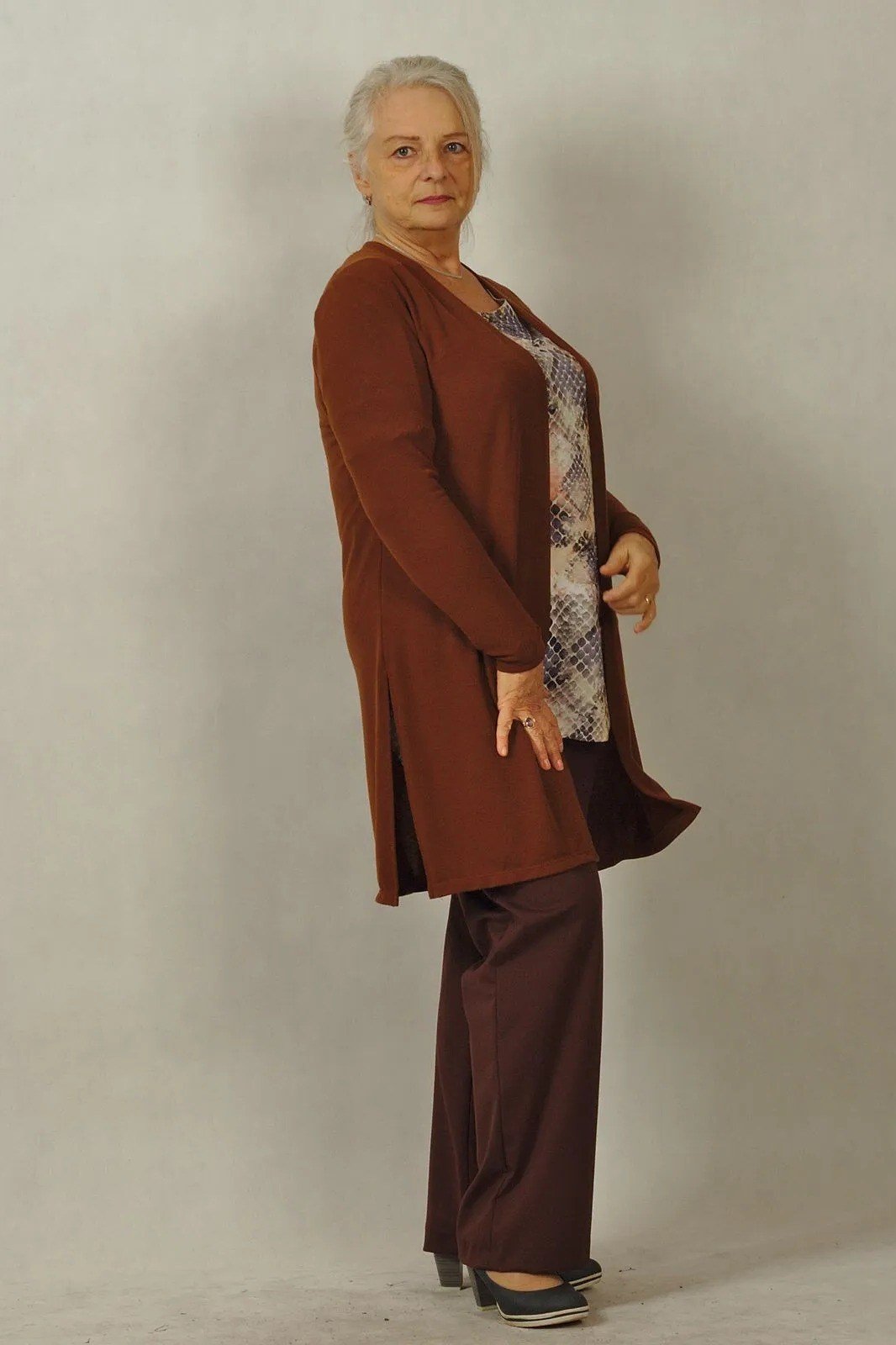 Older woman in a studio wearing a rust cardigan with brown pants