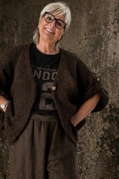 Older woman at a textured wall wearing a dark brown chunky cardigan over a graphic tee